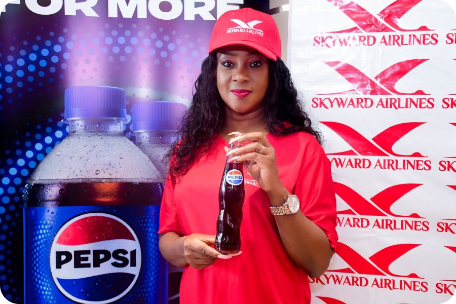 a woman holds a pepsi bottle in front of a pepsico and skyward airlines banner